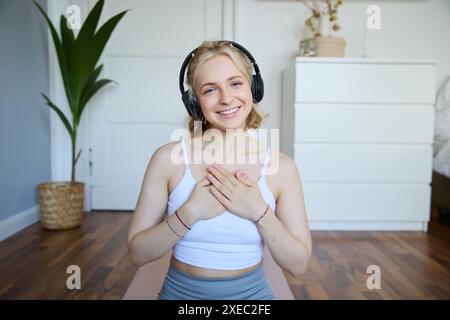 Porträt einer Frau, die sich nach Meditation oder Yoga-Training zu Hause entspannt und in Ruhe fühlt, Hände auf der Brust hält, Kopffoto trägt Stockfoto