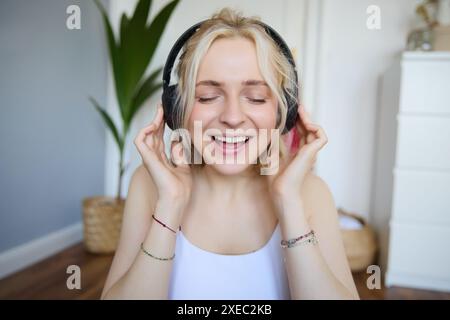 Nahaufnahme eines Porträts einer Frau, die lächelt, während sie Musik in kabellosen Kopfhörern hört und mit geschlossenen Augen singt Stockfoto