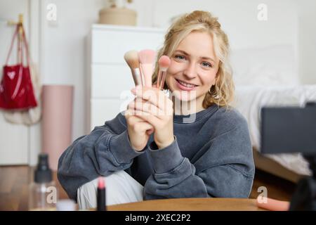 Porträt der Medienschafferin, Bloggerin sitzt in ihrem Zimmer und nimmt Videos ihrer Lieblings-Make-up-Pinsel auf, spricht vor der Kamera Stockfoto