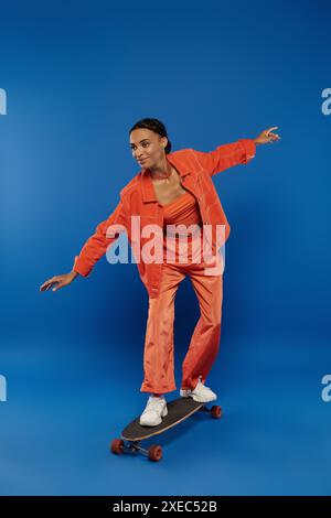 Junge afroamerikanische Frau im orangefarbenen Jumpsuit Skateboarding auf blauem Hintergrund. Stockfoto