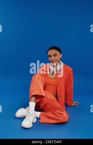 Eine junge Afroamerikanerin in leuchtendem Orange sitzt auf dem Boden und taucht über Kopfhörer in Musik ein. Stockfoto