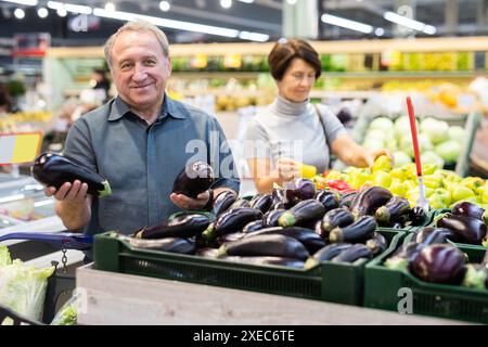 Ein reifer Käufer wählt reife Auberginen im Lebensmittelgeschäft Stockfoto