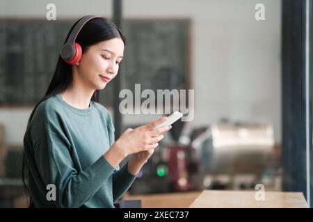 Eine Frau, die Kopfhörer trägt, schaut auf ihr Handy Stockfoto
