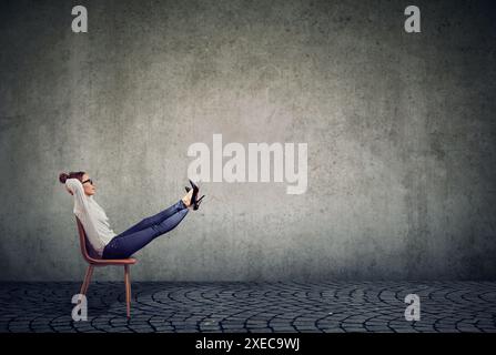 Junge Geschäftsfrau, die in einem Bürostuhl sitzt und ihre Beine hochgehoben hat, tagträumend Stockfoto