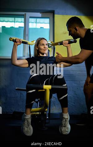 Personal Coach, der die Sportlerin bei der Benutzung des Geräts während des Fitnessstudios in einem dunklen Fitnessstudio unterstützt Stockfoto