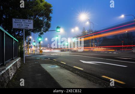 Langzeitbelichtungsbild von Busspuren, die bei starkem Nebel durch grüne Ampeln fahren. Auckland. Stockfoto