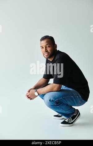 Ein afroamerikanischer Mann in schwarzem Hemd und Jeans kniet vor einer lebendigen Kulisse nieder. Stockfoto