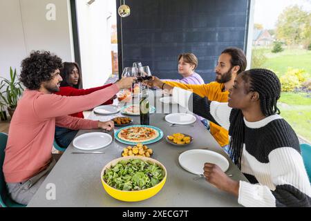 Fröhliches Essen: Freunde heben Gläser in einem gemeinsamen Essen zu Hause Stockfoto