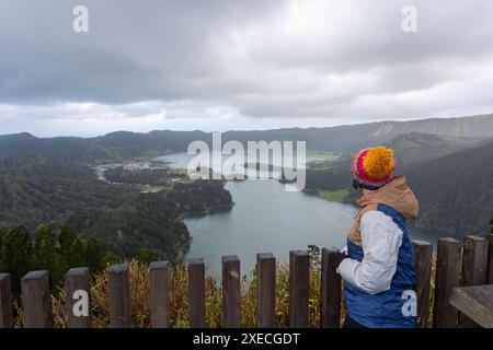 Eine Frau mit farbenfroher Mütze und schwarzer Jacke blickt über den malerischen See Sete Cidades auf der Insel São Miguel auf den Azoren. Der ruhige See, s Stockfoto