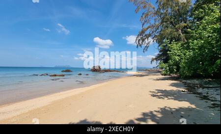 Ein Sandstrand, der sich neben dem glitzernden Meer unter einem klaren blauen Himmel erstreckt und eine ruhige und malerische Szene schafft Stockfoto