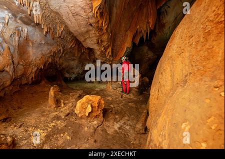 Ein Speläologe mit Helm und Scheinwerfer, der eine Höhle mit reichen Stalaktiten- und Stalagmitenformationen erforscht. Stockfoto