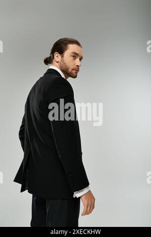 Ein stilvoller bärtiger Geschäftsmann in einem Anzug steht selbstbewusst vor einem grauen Hintergrund in einem Studio-Setting. Stockfoto