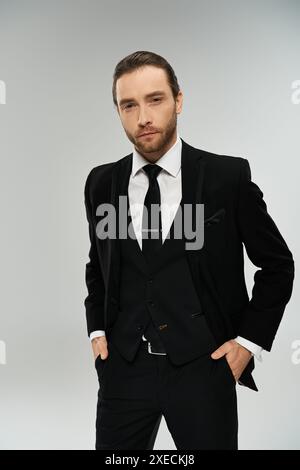 Ein gutaussehender, bärtiger Geschäftsmann in Anzug und Krawatte posiert selbstbewusst vor einem grauen Studio-Hintergrund. Stockfoto