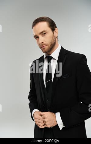 Ein charismatischer, bärtiger Geschäftsmann in einem scharfen Anzug und Krawatte posiert selbstbewusst auf einem grauen Studio-Hintergrund. Stockfoto