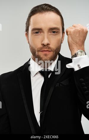 Ein gutaussehender, bärtiger Geschäftsmann in einem eleganten Anzug steht selbstbewusst vor einem grauen Studio-Hintergrund und posiert für ein Porträt. Stockfoto