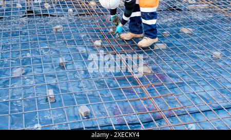 Bauarbeiter, der Stahlbewehrung mit Zangen und Draht auf einer Baustelle befestigt Stockfoto