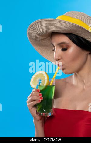 Eine junge Frau trinkt an einem heißen Sommertag einen Drink und hat einen Hut auf dem Kopf. Stockfoto