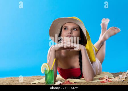 Ein junger Teenager liegt am Strand mit einem alkoholischen Getränk und sonnt sich in der Sommersonne. Stockfoto