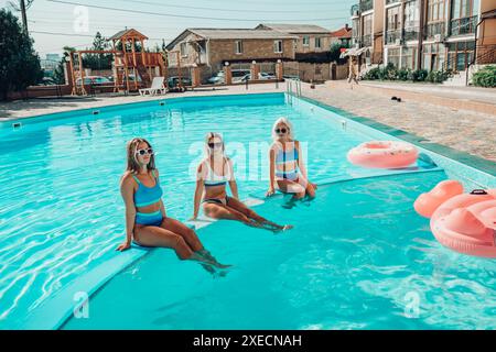 Drei Frauen sitzen in einem Pool mit rosafarbenen und blauen Schwimmbahnen. Die Szene ist unbeschwert und lustig. Stockfoto