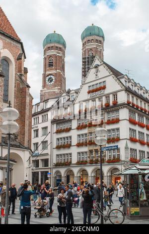 München, Deutschland - 27. Juli 2017: Eine geschäftige Straßenszene vor den ikonischen Doppeltürmen der Kathedrale unserer lieben Lieben Frau. Stockfoto