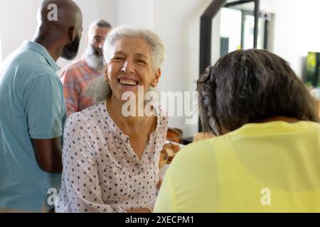 Lächelnde Seniorin genießt die Zeit mit verschiedenen Freunden zu Hause Stockfoto