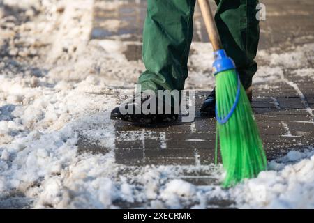 Eine Nahaufnahme, während ein Arbeiter den Straßenbelag nach draußen fegt Von losem Schnee Stockfoto