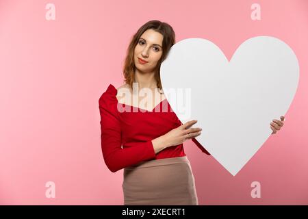 Mädchen mit einer großen weißen Herzform in den Händen. Eine verliebte Studentin steht und hält eine große Herzform in ihren Händen. Valentinstag Stockfoto