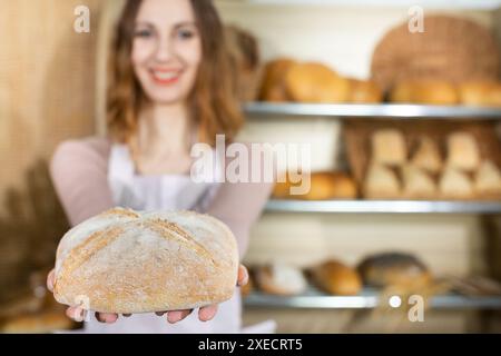 Eine attraktive junge Verkäuferin hält einen Brotlaib in den Händen. Familienbäckerei mit Tradition mehrerer Generationen. Stockfoto