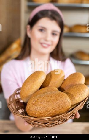 Eine junge Erwachsene und attraktive Bäckerei-Verkäuferin präsentiert im Markengeschäft einer traditionellen, renommierten Familie einen Rollenkorb Stockfoto