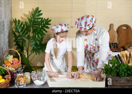 Mom und Tochter Rollen Pizza-Teig mit einem Holzstift auf einem Brett in der Küche aus. Mutter und Baby machen den Teig Stockfoto