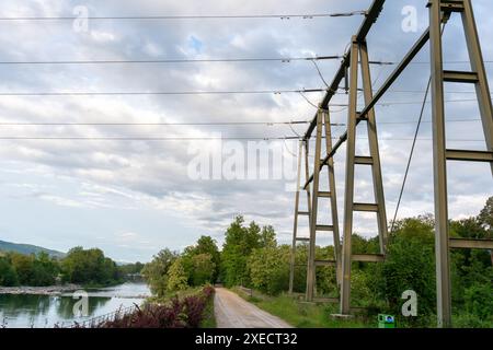 Masten, die Hochspannungskabel in der Nähe eines Wasserkraftwerks transportieren. Ein schöner Fluss, der zur Stromerzeugung genutzt wird, ist in der Nähe zu sehen. Stockfoto