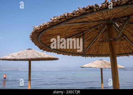 Großer Schilfschirm an einem Strand auf Korfu in Griechenland, mit ruhigem tiefblauem Meer. Stockfoto