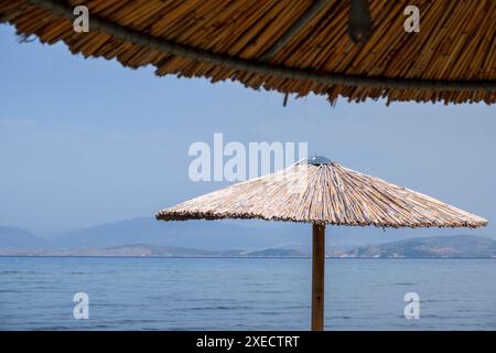 Großer Schilfschirm an einem Strand auf Korfu in Griechenland, mit ruhigem tiefblauem Meer. Stockfoto