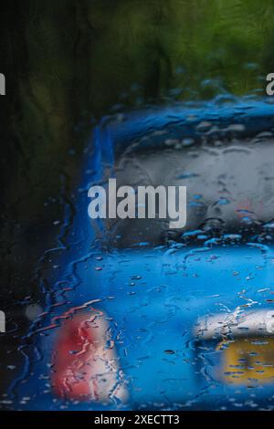 Ein leeres blaues Auto parkt am Straßenrand, durch eine regenbedeckte Windschutzscheibe gesehen. Stockfoto