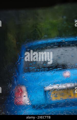 Ein leeres blaues Auto parkt am Straßenrand, durch eine regenbedeckte Windschutzscheibe gesehen. Stockfoto