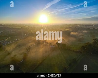 Landschaftsfotografie der Stadt Cirencester in den Cotswolds während der Sonnenaufgang über nebeligen Feldern. Stockfoto