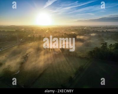 Landschaftsfotografie der Stadt Cirencester in den Cotswolds während der Sonnenaufgang über nebeligen Feldern. Stockfoto