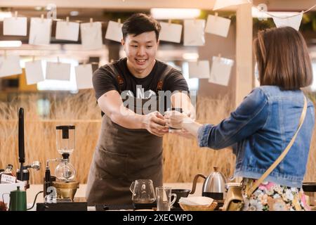 Asiatischer Mann, Kaffeemaschine, Übergabe einer Tasse Kaffee an weibliche Kunden Theke, Startup Business Konzept. Stockfoto