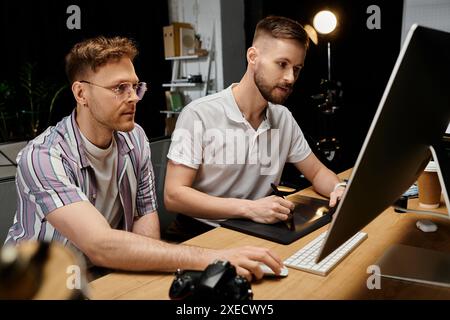 Zwei Männer in lässiger Kleidung arbeiten zusammen an einem Laptop am Schreibtisch. Stockfoto