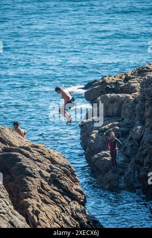 Ein junger Mensch springt von einer felsigen Klippe ins Meer in Ouistreham, Bretagne, Frankreich, und vermittelt ein Gefühl von Abenteuer und Spannung. Stockfoto