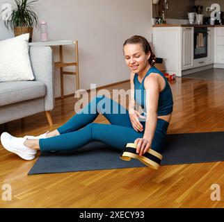 Workout zu Hause. Frau sitzt auf der Trainingsmatte mit Mini-Widerstandsband in der Hand. Stockfoto