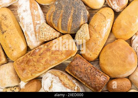 Viele Brotsorten und Brötchen, die zufällig nebeneinander auf einer hölzernen Arbeitsplatte als Dekoration einer traditionellen Bäckerei platziert werden Stockfoto
