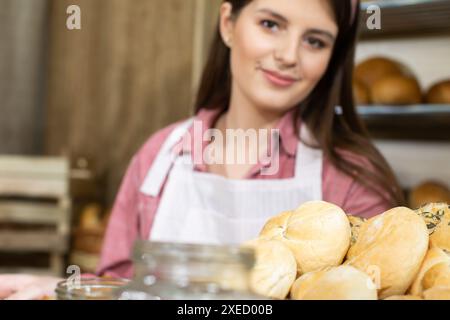 Eine junge Erwachsene und attraktive Bäckerei-Verkäuferin präsentiert im Markengeschäft einer traditionellen, renommierten Familie einen Rollenkorb Stockfoto