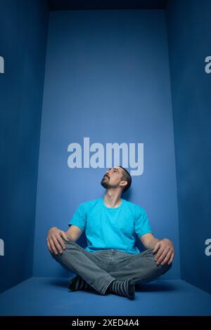 Ein Mann in blauem Hemd sitzt im blauen Zimmer mit überkreuzten Beinen Stockfoto