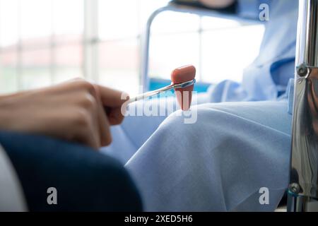 Ein Arzt verwendet einen Reflexhammer, um das Kniegelenk eines Patienten zu beurteilen Stockfoto