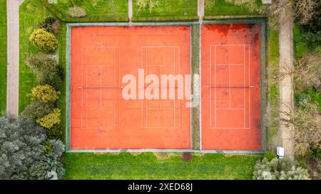 Blick aus der Vogelperspektive auf Twin Red Clay Tennisplätze, umgeben von Grün Stockfoto