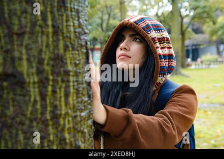 Glückliche junge Frau mit Ausdruck der Ruhe und Bewunderung berührt den Baum mit ihren Händen und fühlt Ruhe durch Rinde. Sie steht da Stockfoto