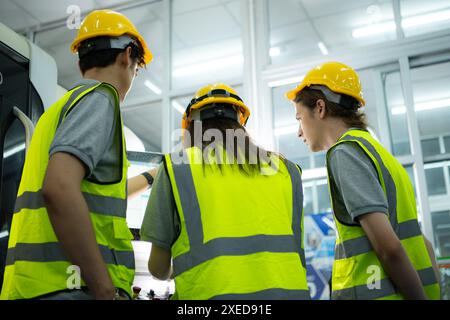 Rückansicht eines jungen Fabrikarbeiters mit Schutzhelm, der auf einen Computerbildschirm blickt, der die Produktion steuert. Stockfoto