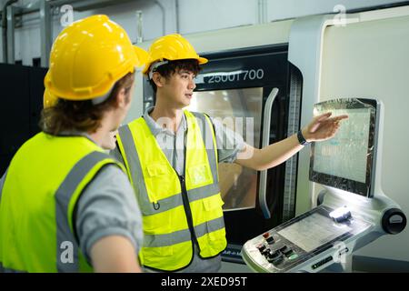 Rückansicht eines jungen Fabrikarbeiters mit Schutzhelm, der auf einen Computerbildschirm blickt, der die Produktion steuert. Stockfoto