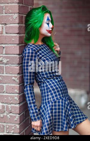 Porträt eines grünhaarigen Mädchen in gechert Kleid mit Joker Make-up auf einer Ziegelwand verschwommen Hintergrund. Stockfoto